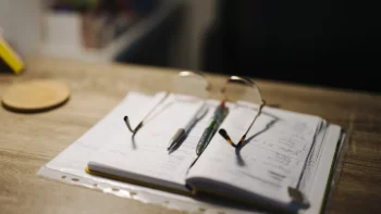 Carnet ouvert avec des notes manuscrites, deux stylos et des lunettes sur un bureau